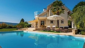 Une grande maison avec une piscine, un patio couvert et une vue sur les montagnes.