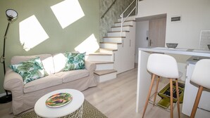 A modern living space with a staircase, a sofa with tropical pillows, a dining area with bar stools, and a kitchen counter. - Palms Apartments Budapest (Budapest)