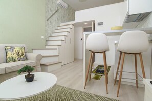 Uma sala de estar moderna com escada, um sofá com almofada decorativa, uma pequena mesa com uma planta e dois banquetes.