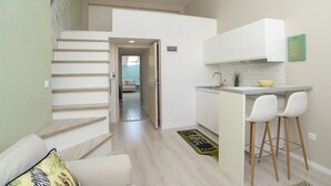 A modern kitchen with white cabinets, a small island with bar stools, and a staircase leading to another room. - Palms Apartments Budapest (Budapest)