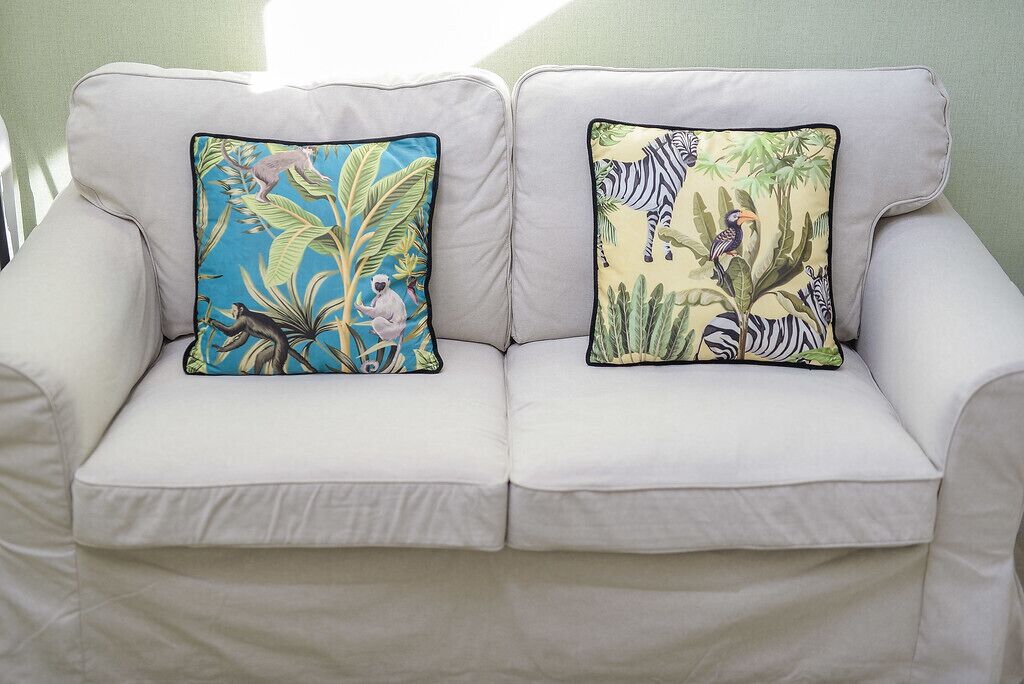 A white sofa with two decorative pillows featuring animal and plant patterns.
