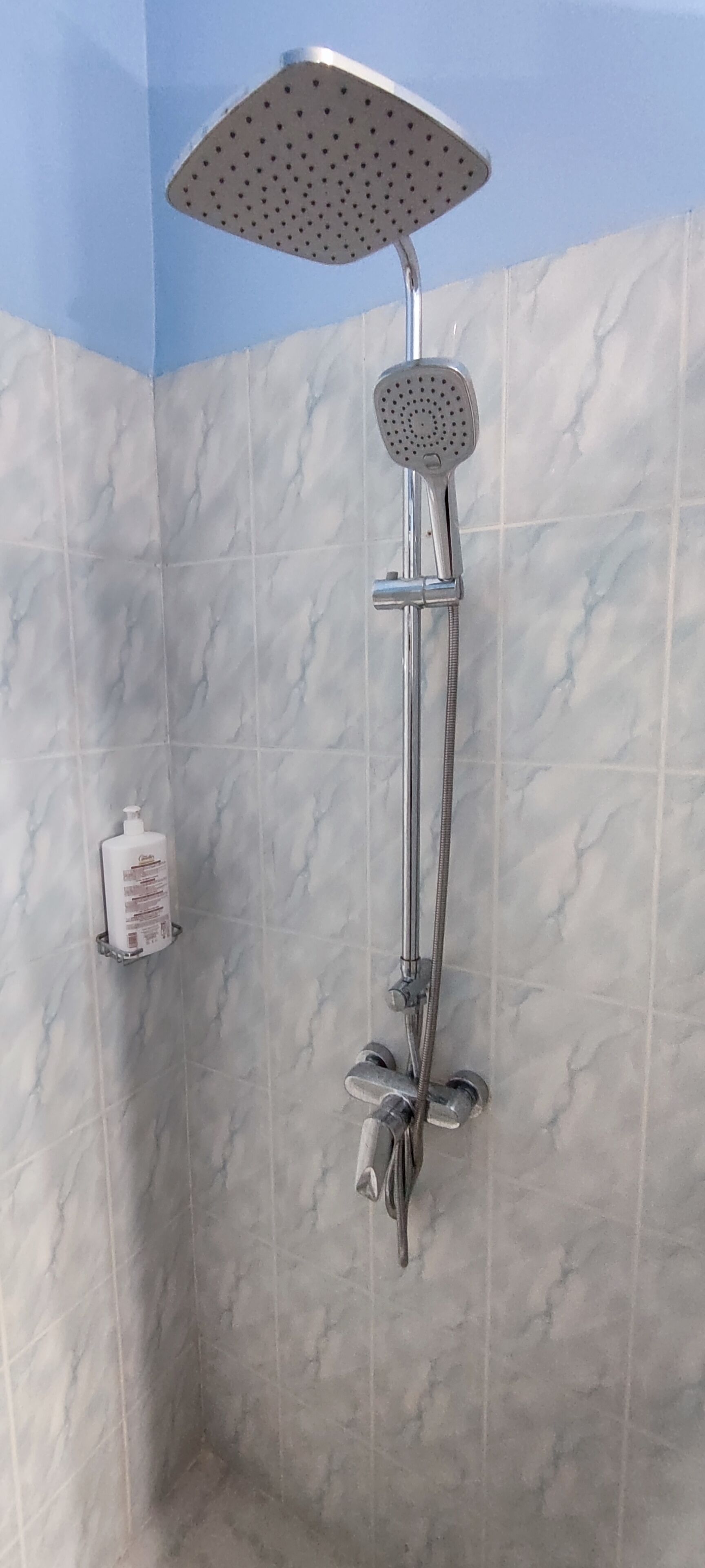 A shower with a handheld showerhead and a fixed showerhead, mounted on a wall with a marble-like texture.