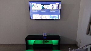 Seinälle asennettu televisio, musta viihdekeskus, jossa on vihreä valaistus, ja osittain näkyvissä oleva verho.