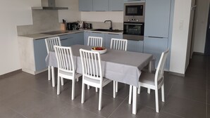 A modern kitchen with grey cabinets, a built-in oven, and a dining table with white chairs. - 6/8 person apartment, large terrace (Porto-Vecchio)