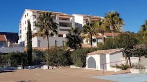 A multi-story building with a tiled roof, surrounded by palm trees and a parking area. - 6/8 person apartment, large terrace (Porto-Vecchio)