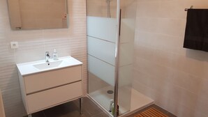 A modern bathroom with a glass shower enclosure, a white sink with a mirror above, and a black towel hanging on the wall. - 6/8 person apartment, large terrace (Porto-Vecchio)