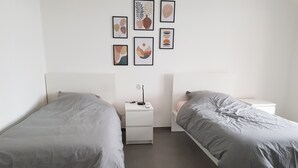 A bedroom with two beds, a nightstand with a lamp, and framed artwork on the wall. - 6/8 person apartment, large terrace (Porto-Vecchio)