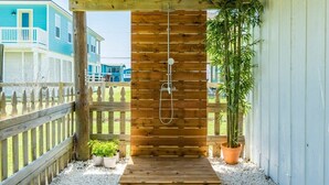 Eine Holzterrasse mit Dusche, umgeben von einem Holzzaun, Pflanzgefäßen und Blick auf benachbarte Häuser.