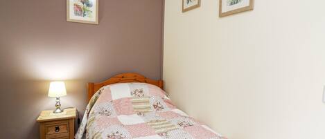 A bedroom with a wooden bed, a bedside table with a lamp, and two framed pictures on the wall.