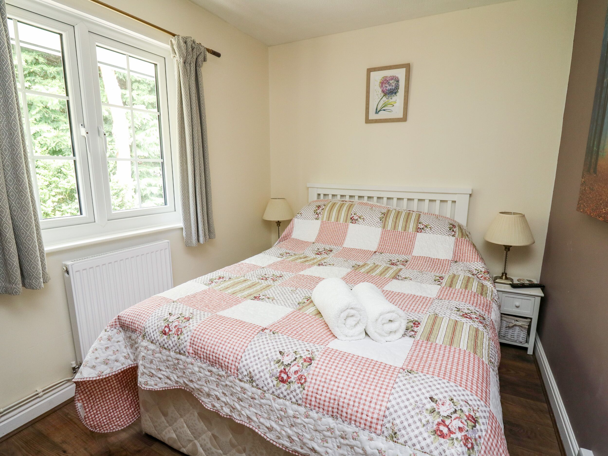 A neatly made bed with a floral quilt, a bedside lamp, and a window with curtains.