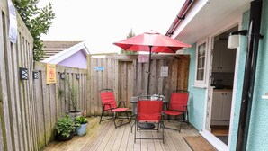 Una terraza de madera con mesa y sillas, un paraguas rojo y un letrero de precaución por piso mojado.
