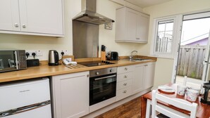 A compact kitchen with white cabinets, a stainless steel range hood, a built-in oven, and a microwave. - Primrose Cottage (Llandrindod Wells)