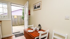 A dining area with a wooden table and white chairs, a framed picture on the wall, and a fire extinguisher mounted on the wall. - Primrose Cottage (Llandrindod Wells)