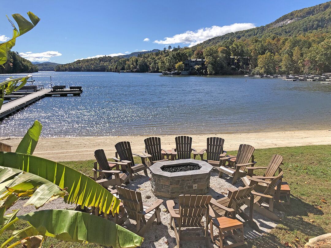 A lakeside deck with Adirondack chairs and a stone fire pit.