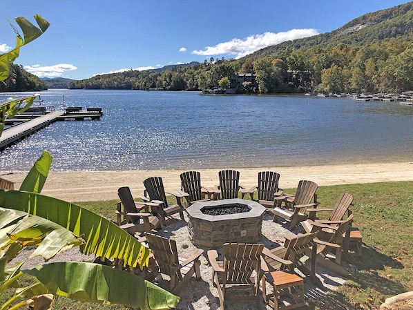 A lakeside deck with Adirondack chairs and a stone fire pit.