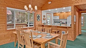 A wooden cabin interior with a dining area, kitchen, and large windows. - Cabin Near Leavenworth - Deck + Pets Free (Leavenworth)