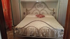 A bed with a metal frame and a white mattress, a red pillow, and a patterned bedspread. - Apartment (Santa Teresa Gallura)