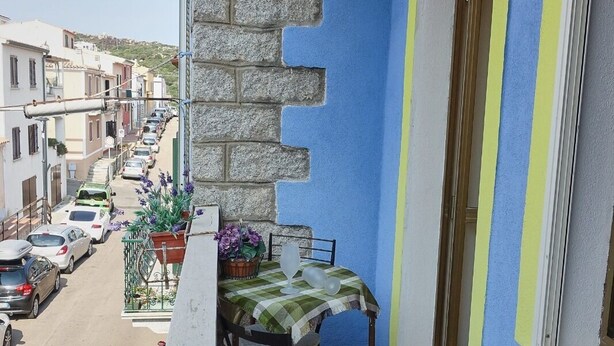 A balcony with a table and chairs, a stone wall, a blue wall, and a door with yellow trim. - Apartment (Santa Teresa Gallura)
