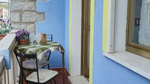 A balcony with a table and chairs, a potted plant, and a window with a view. - Apartment (Santa Teresa Gallura)