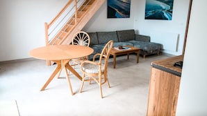 Una sala moderna con una escalera de madera, un sofá gris, una mesa de comedor de madera con sillas y dos cuadros en la pared.