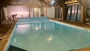Una piscina interior con agua cristalina, cubierta de madera y techo alto con vigas a la vista.
