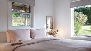 A bedroom with a large window, a bed with a beige comforter, a bedside table with a lamp, and a framed artwork on the wall. - Brandy Hot Forest Retreat - 16 guests | Free Wifi (Eganstown)