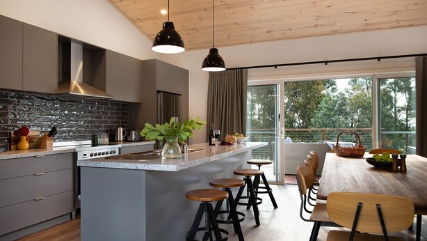 Cocina moderna con una isla central, taburetes de bar y un comedor con vistas al exterior.