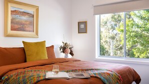 Un dormitorio con una cama grande, una ventana que da a árboles y un cuadro en la pared.