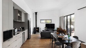 Eine moderne Küche mit grauen Schränken, einem eingebauten Backofen und einem schwarzen Herd. Es gibt einen Essbereich mit einem dunklen Holztisch, Stühlen und einem Fernseher darüber.