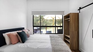 Une chambre avec une grande fenêtre, un lit avec une literie blanche, une armoire en bois et une vue sur l’extérieur.
