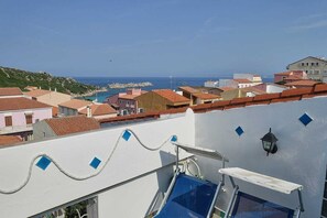 A coastal town with terracotta-roofed buildings, a white wall with a blue railing, and a clear view of the sea. - Beachfront Lofts (Santa Teresa Gallura)