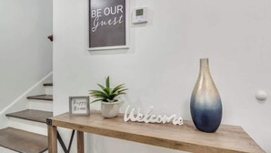 En træreception med en velkomstskilt, et skilt med teksten 'Happy Home', en potteplante og en vase.
