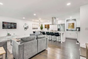 A modern living space with a grey sofa, a kitchen area, and a dining bar.