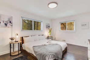 A bedroom with a large bed, two bedside tables, a bedside lamp, and a window with blinds.