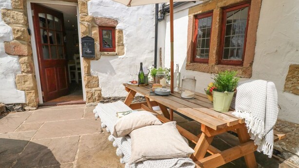 A stone building with a wooden table and benches, a door, and a window. - Hope Cottage (Bakewell)