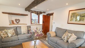 A cozy living room with two grey sofas, a wooden coffee table, and a vase with flowers. - Hope Cottage (Bakewell)