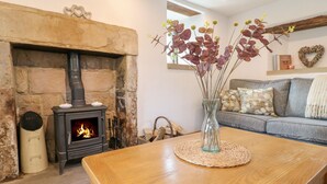 A cozy living room with a stone fireplace, a wooden table, and a vase with dried flowers. - Hope Cottage (Bakewell)
