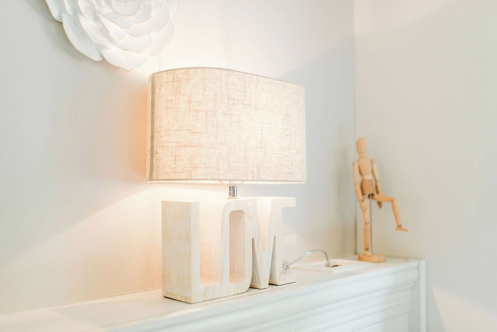 A lamp with a textured shade on a white stand, a white wall, and a wooden mannequin.