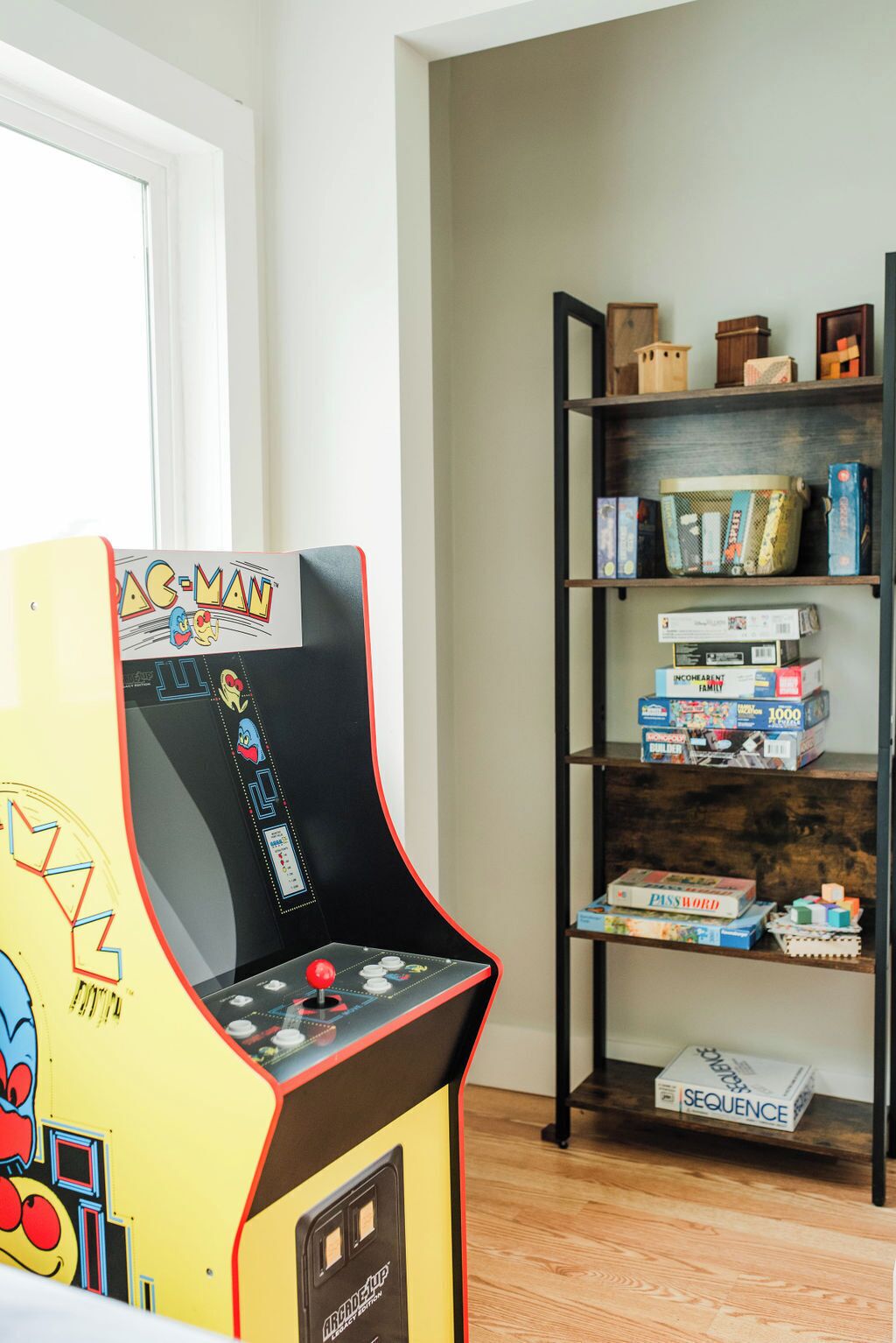 An arcade machine with a colorful design, a bookshelf with various board games, and a door in the background.