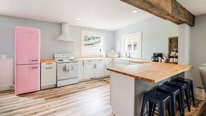 Una cocina moderna con armarios blancos, un refrigerador rosa, encimeras de madera y una isla central con taburetes.