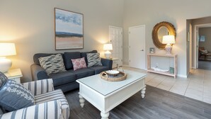 Uma sala de estar com sofá, poltrona, mesa de centro e um quadro na parede.