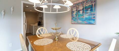A dining area with a wooden table, white chairs, a chandelier, and a painting of boats on the wall.