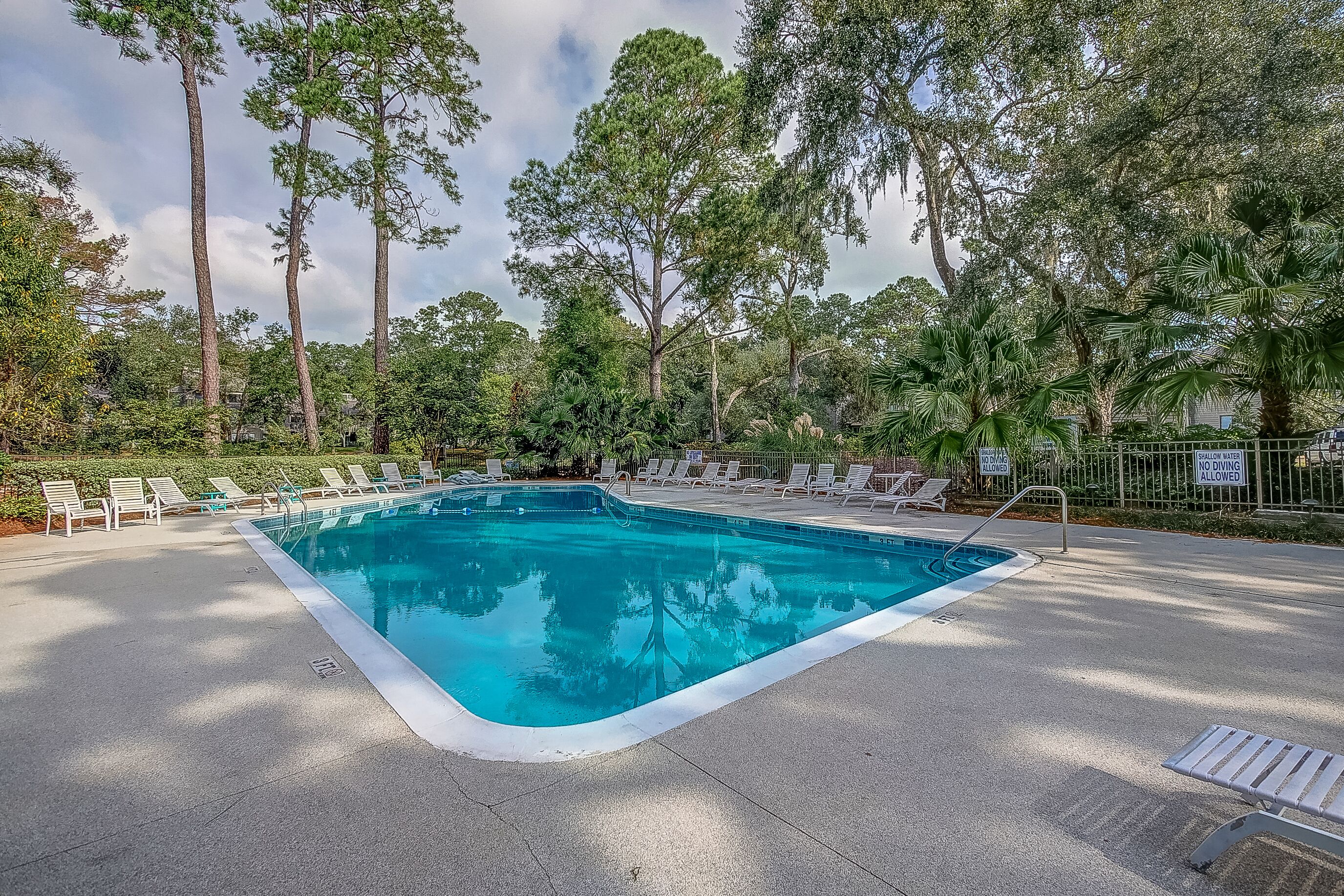 A rectangular pool with a white edge, surrounded by lounge chairs and a fence.
