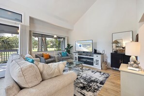A modern living room with a sofa, television, and a view of the outdoors.
