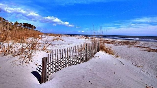 A beach with a wooden fence and sand dunes.