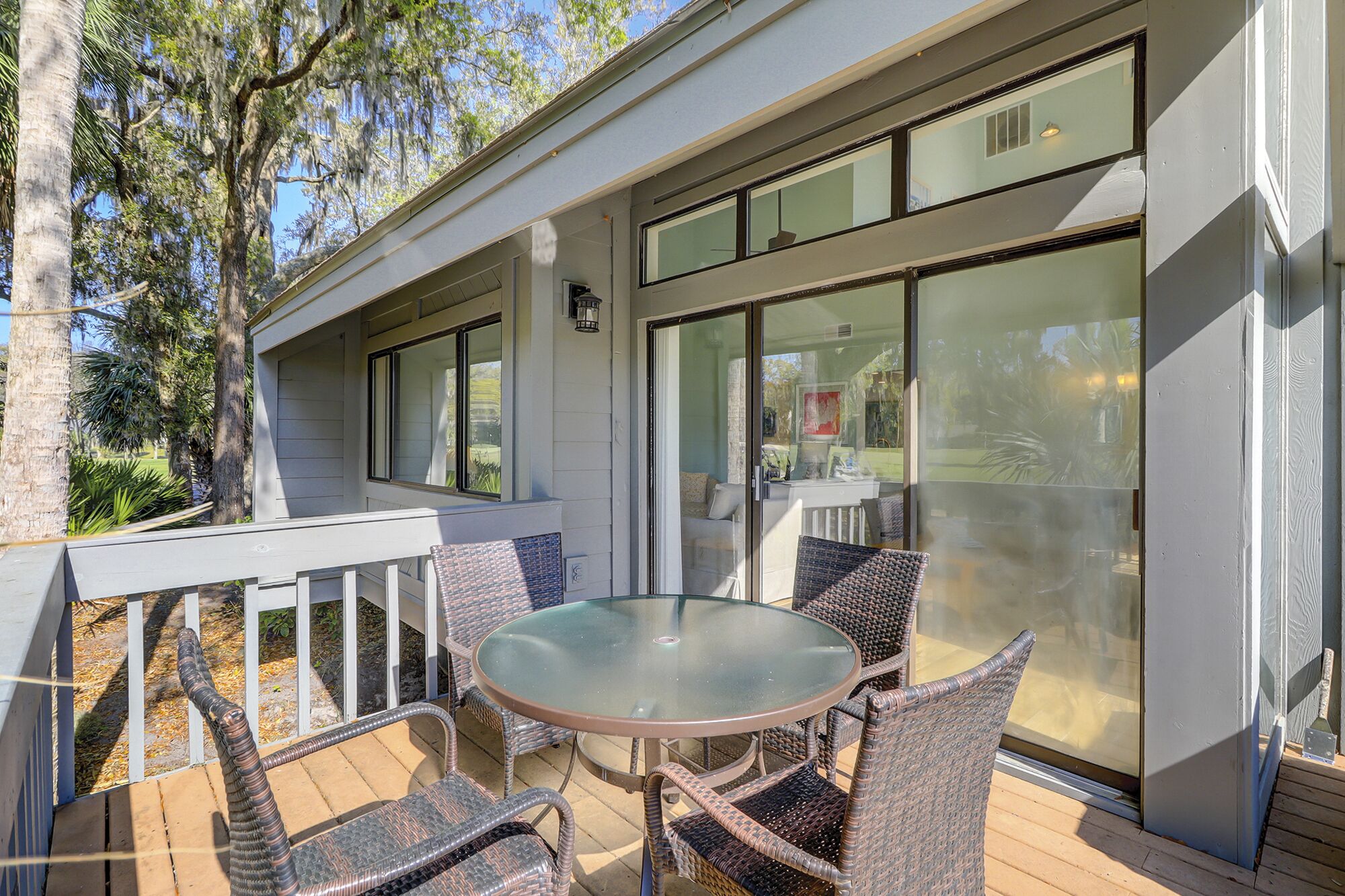 Une terrasse couverte avec une table en verre et des chaises en osier, de grandes fenêtres et une balustrade blanche.