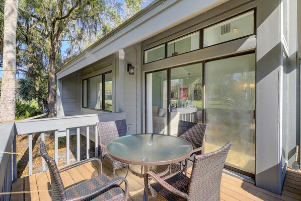 A covered patio with a glass table and wicker chairs, large windows, and a white railing.