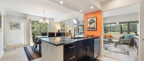A modern kitchen with a central island, dark cabinetry, and a view to the living area.