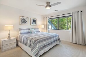 A bedroom with a bed, nightstands, a ceiling fan, a window with curtains, and two wall art pieces.