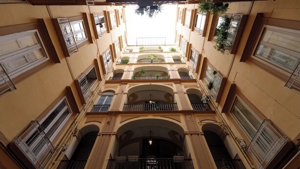 A multi-story building with balconies, arched doorways, and hanging plants.
